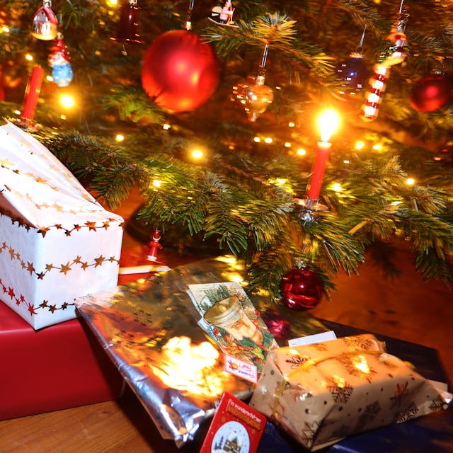 Man sieht den Fuß eines geschmückten Weihnachtsbaum, darunter liegen eingepackte Geschenke.