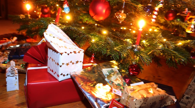Man sieht den Fuß eines geschmückten Weihnachtsbaum, darunter liegen eingepackte Geschenke.