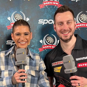Florian Hempel posiert vor seinem Zweitrunden-Auftritt bei der Darts-WM im TV-Studio mit Sport1-Moderatorin Jana Wosnitza.