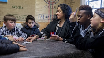 Kinder und eine Betreuerin spielen Karten an einem Tisch.
