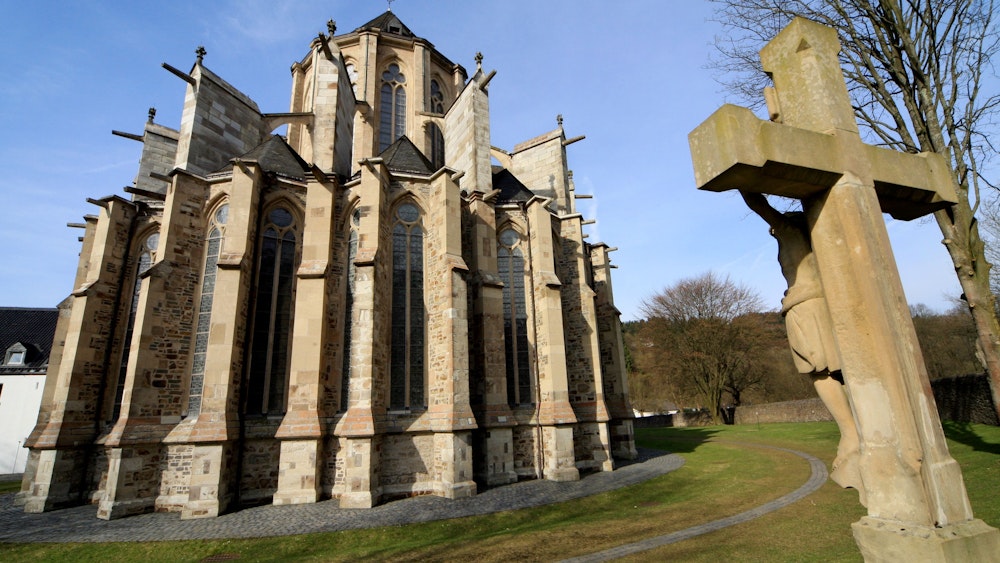 Ein Steinkreuz steht vor dem gotischen Dom von Altenberg.