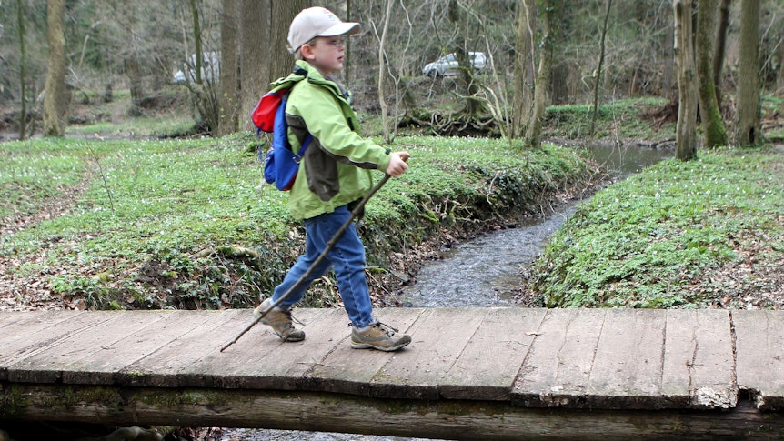 Ein Kind geht mit einem Wanderstock und Rucksack über einen Steg.