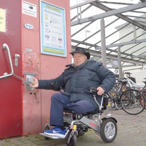 Der Rollstuhlfahrer Wilhelm Hachenberg vor einer geschlossenen Toilette am Bahnhof Euskirchen. An der Tür hängt eine Kette mit einem Vorhängeschloss.