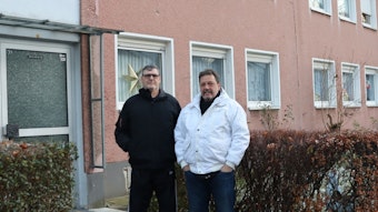 Zwei Männer vor einem rötlichen Mietshaus der Siedlung.