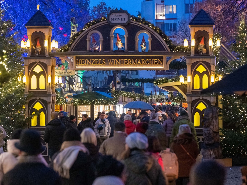 Menschen gehen auf den Weihnachtsmarkt: Auf einem Schild steht Heinzels Wintermärchen.