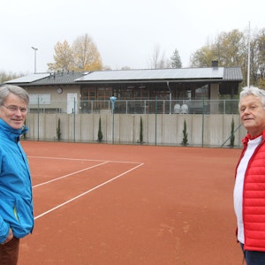 Zwei Männer in blauer und roter Jacke stehen auf einem Tennisfeld.