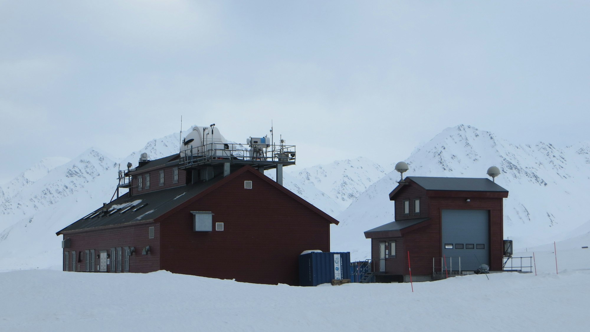 In Ny Alesund auf Spitzbergen liegt eine deutsch-französische Forschungsstation zur Untersuchung des Klimawandels in der Arktis. Das Bild zeigt zwei dunkelrote Häuser mit Antennen und technischen Instrumenten auf dem Dach.