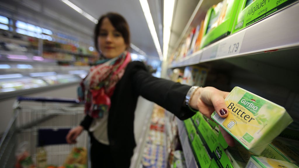Eine Frau nimmt in einem Supermarkt von Aldi (Nord) Bio-Butter aus dem Regal.