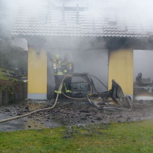 Feuerwehrleute löschen einen Brand an einem Carport.