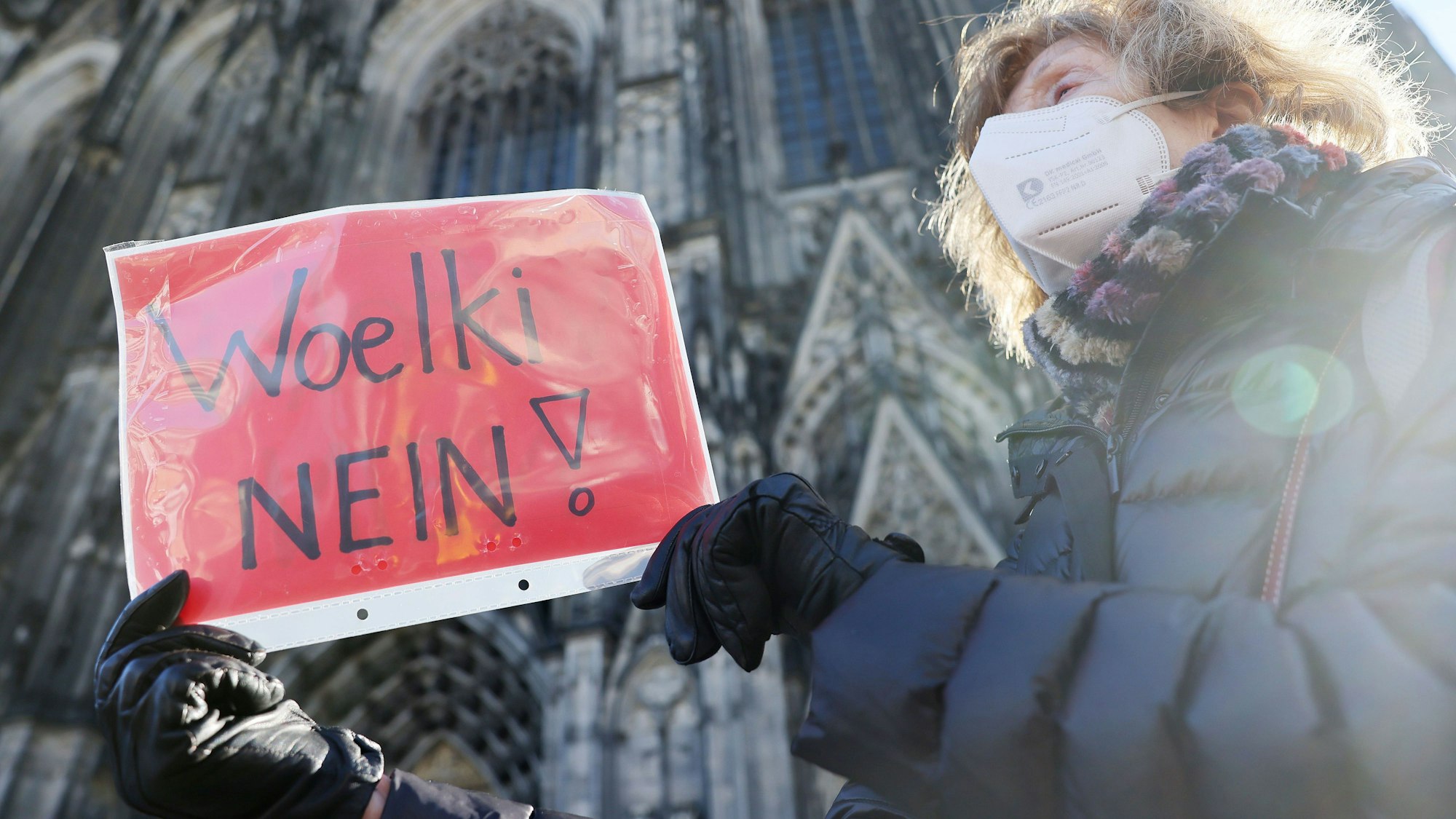 Eine Frau nimmt mit einem Plakat mit der Aufschrift „Woelki Nein!“an einer Kundgebung der kirchenkritischen Bewegung Maria 2.0 gegen Kardinal Rainer Maria Woelki teil. Im Hintergrund ist der Kölner Dom zu sehen.