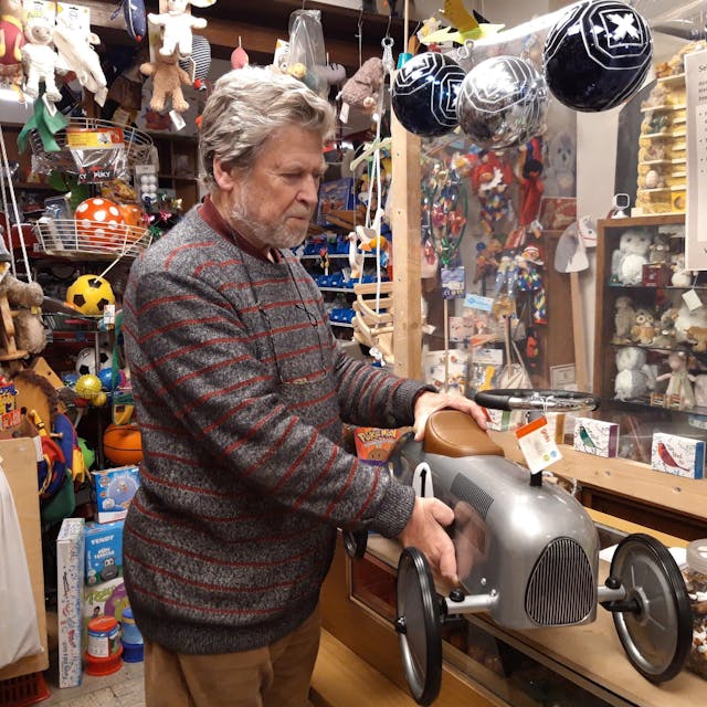 Inhaber Dieter van Dillen hält in seinem Laden ein silbernes Rutschauto in der Hand.
