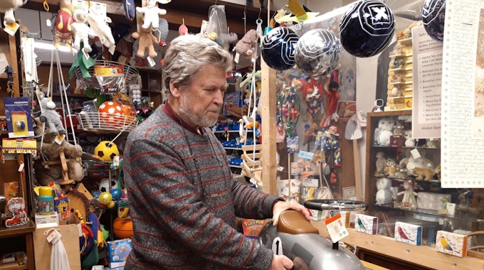 Inhaber Dieter van Dillen hält in seinem Laden ein silbernes Rutschauto in der Hand.