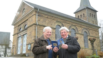 Pfarrer Ralph Knapp (l.) und Autor Otto Dinger stehen vor der Kirche in Delling und halten das Buch von Dinger in den Händen.
