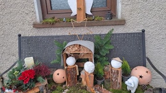 Auf einer Gartenbank steht eine aus Holzstämmen und Tonkugeln gefertigte Krippe.
