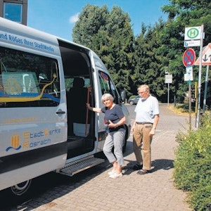 Eine Frau und ein Mann wollen an der Haltestelle Bitze in den Rö-Bus, den weißen Rösrather Bürgerbus, einsteigen.