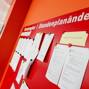 Auf einer roten Tafel mit der Überschrift „Stundenplan - Stundenplanänderung“ hängen zahlreiche Mitteilungen im DIN-A4-Format.