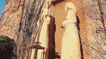 Zwei große Holzfiguren stehen vor einer steinernen Kirche.