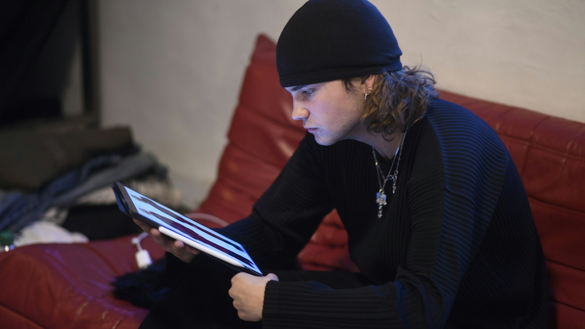 Luis Dobbelgarten sitzt mit iPad auf einem roten Sofa.