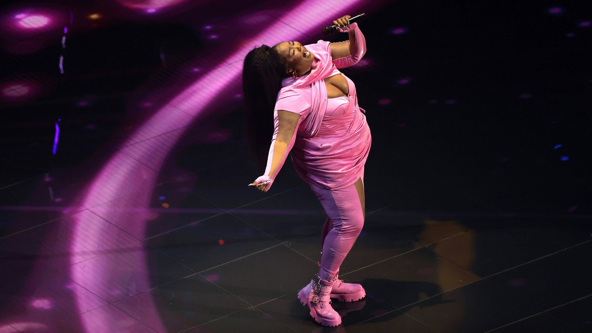 Lizzo steht im rosa Kostüm auf einer Bühne und singt.