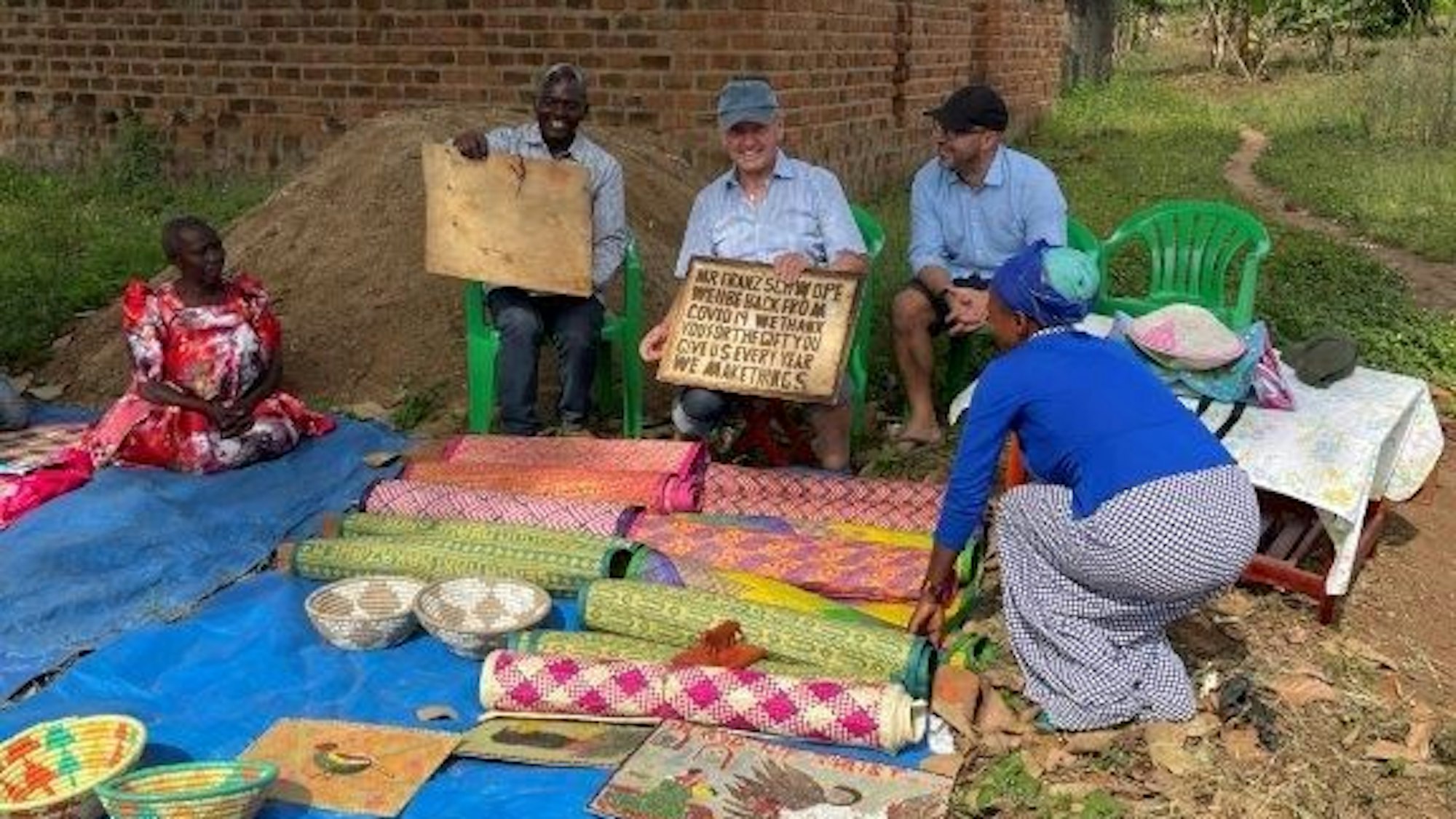 Franz Schwope inmitten von Menschen aus Uganda, vor ihnen bunte Decken und Matten