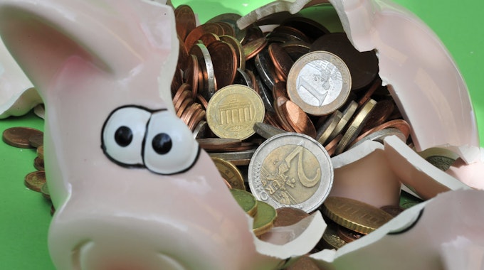Ein Sparschwein liegt verschlagen auf einer grünen Oberfläche, es sind Geldmünzen in dem Schwein.