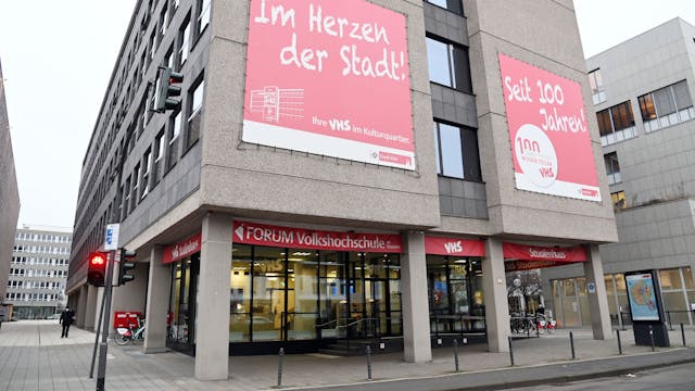 Das Gebäude der Volkshochschule in Köln, auf Plakaten an der Wand steht: „Im Herzen der Stadt!“ und „Seit 100 Jahren!“.