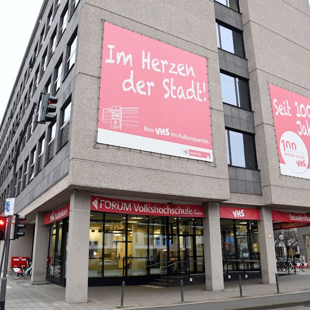 Das Gebäude der Volkshochschule in Köln, auf Plakaten an der Wand steht: „Im Herzen der Stadt!“ und „Seit 100 Jahren!“.