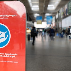 Ein Schild mit der Aufschrift „Bitte Mund-Nase-Bedeckung tragen!“ steht auf einem Schild am Eingang im Hauptbahnhof. In den Fernzügen der Bahn gilt noch immer die Maskenpflicht.