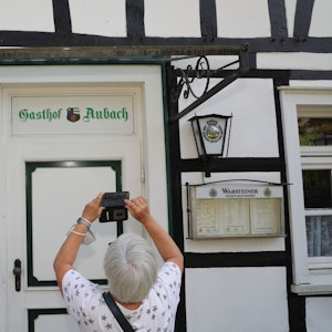 Eine Frau fotografiert mit ihrem Handy den Schriftzug „Gasthof Aubach“ an der Tür des Fachwerkhauses in Kürten-Olpe-