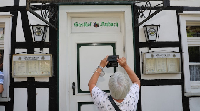 Eine Frau fotografiert mit ihrem Handy den Schriftzug „Gasthof Aubach“ an der Tür des Fachwerkhauses in Kürten-Olpe-