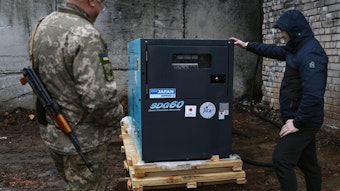 Ein Mann und ein Soldat betrachten einen von Japan gespendeten Stromgenerator.