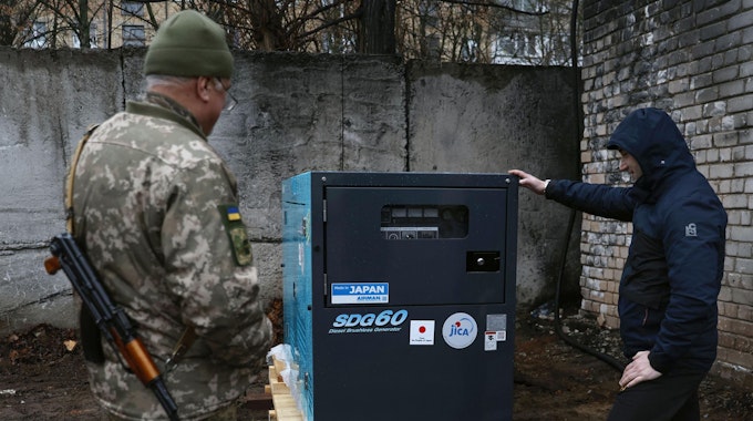 Ein Mann und ein Soldat betrachten einen von Japan gespendeten Stromgenerator.