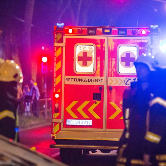 Ein Rettungswagen steht vor mehreren Feuerwehrleuten an einer Einsatzstelle in Köln. (Symbolbild)