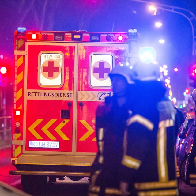 Ein Rettungswagen steht vor mehreren Feuerwehrleuten an einer Einsatzstelle in Köln. (Symbolbild)
