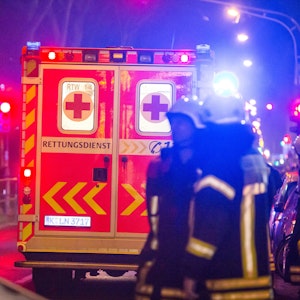 Feuerwehrleute stehen nachts hinter einem Rettungswagen.