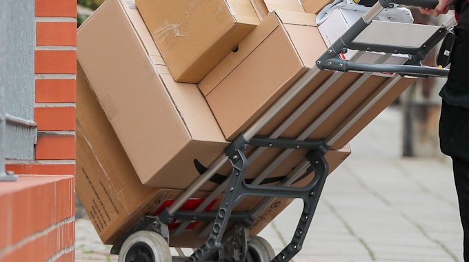 Ein DHL Paketzusteller geht mit einer Sackkarre voll Pakete zu einem Haus.