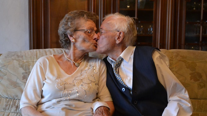 Eheleute Anna und Harry Spangenberg sitzen auf einer Couch und küssen sich.