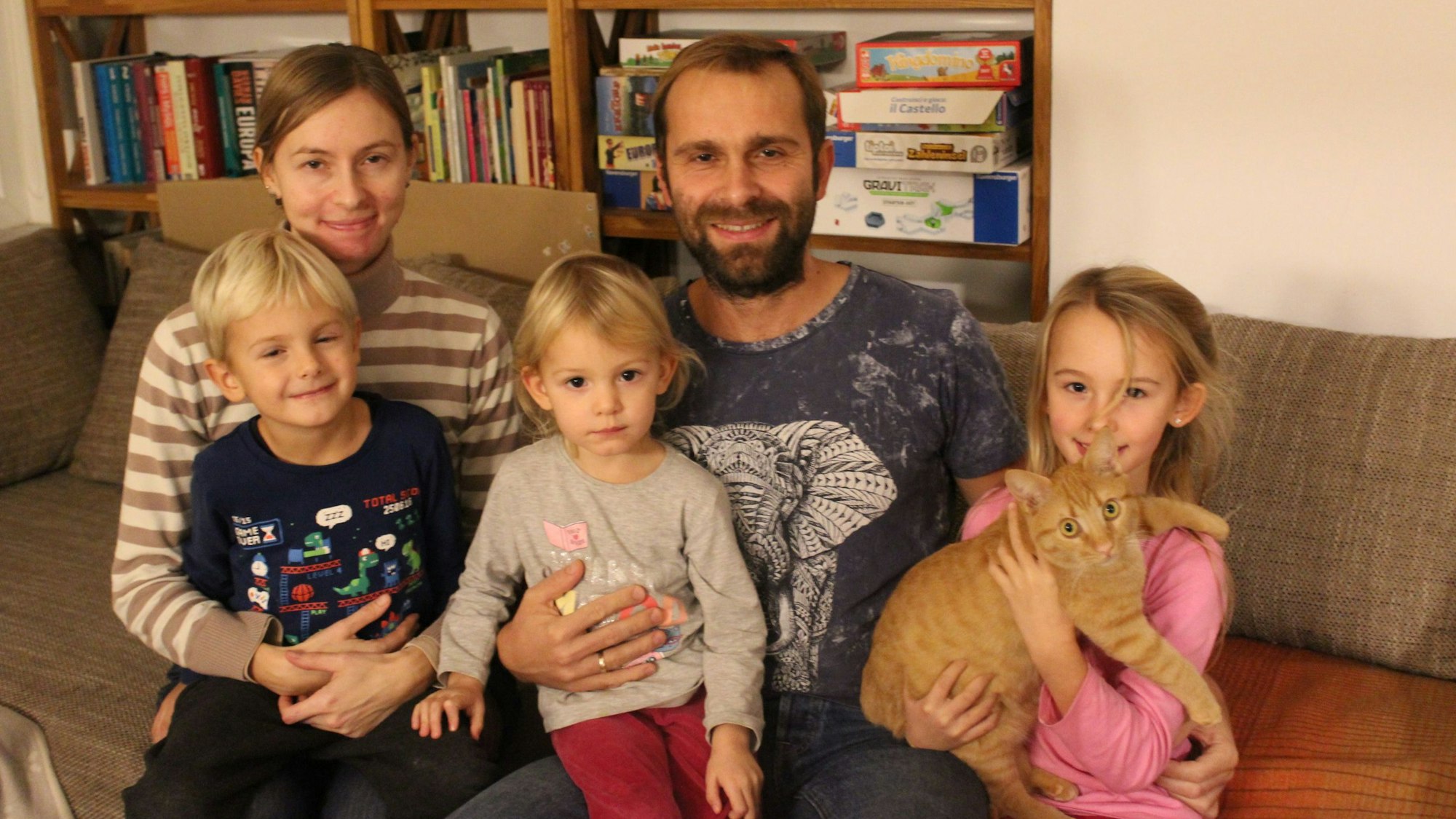 Justina und Przemyslaw Cwiecek sitzen mit ihren Kindern Anton, Sofia und Greta auf dem Sofa. Tochter Greta hält Kater Teo auf dem Arm.