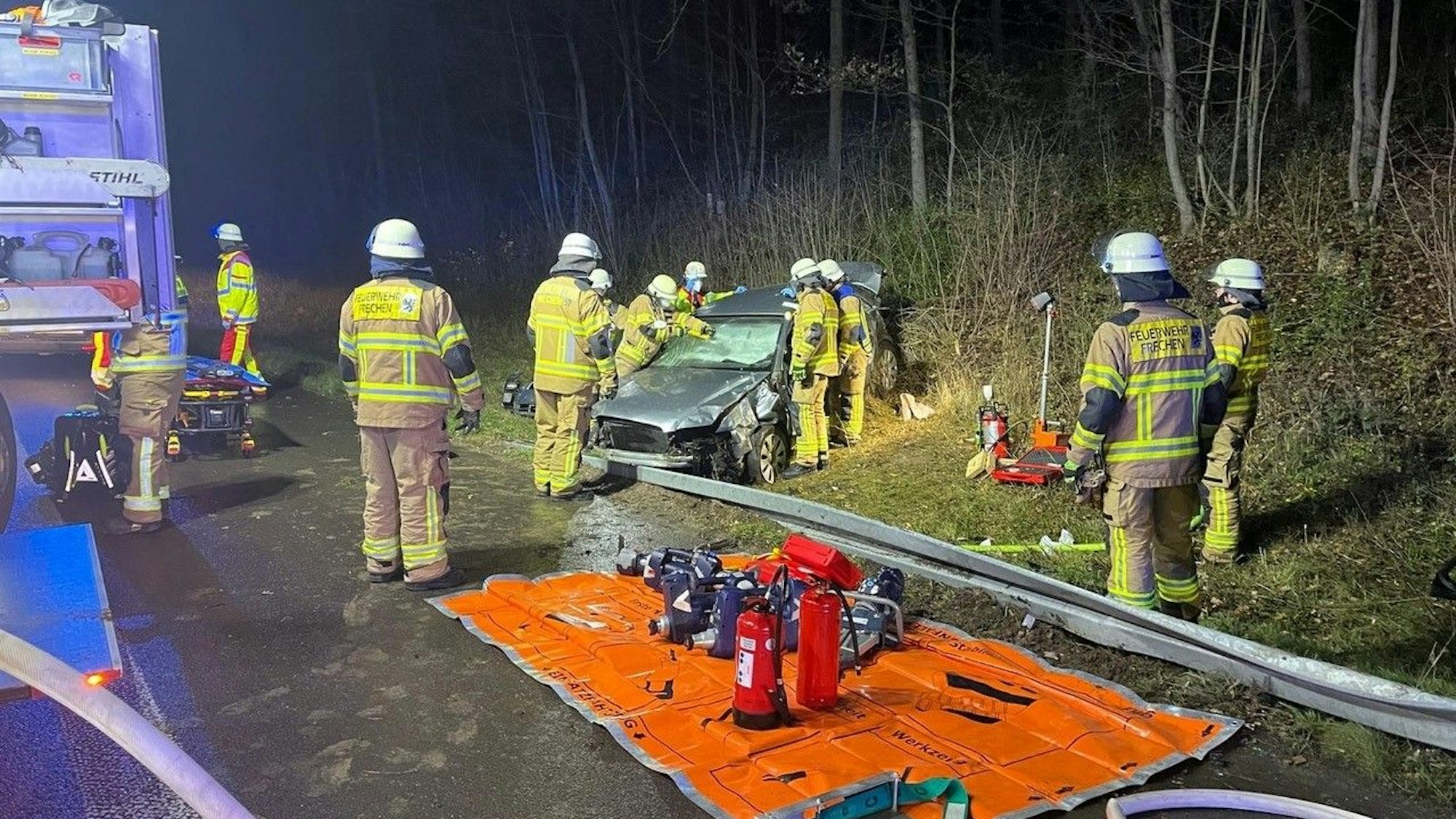 Bei einem Unfall bei Hürth sind zwei Personen verletzt worden, Feuerwehrleute stehen an einem Auto, das im Grünstreifen neben der Fahrbahn steht, es ist stark beschädigt.