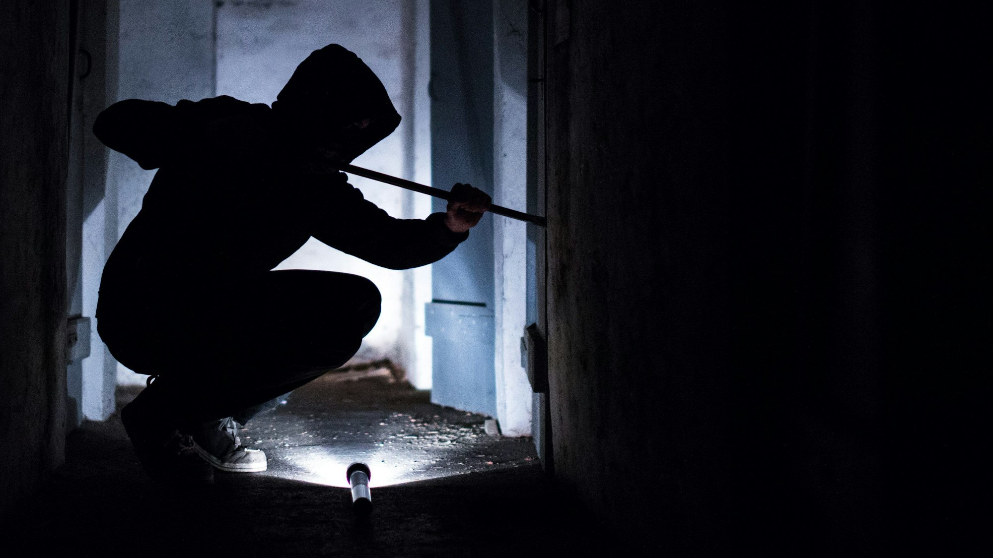 Ein Mann hebelt mit einem Brecheisen eine Tür im Keller eines Wohnhauses auf (gestellte Szene).