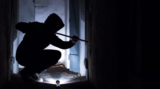 Ein Mann hebelt mit einem Brecheisen eine Tür im Keller eines Wohnhauses auf (gestellte Szene). Foto: Silas Stein/dpa +++ dpa-Bildfunk +++
