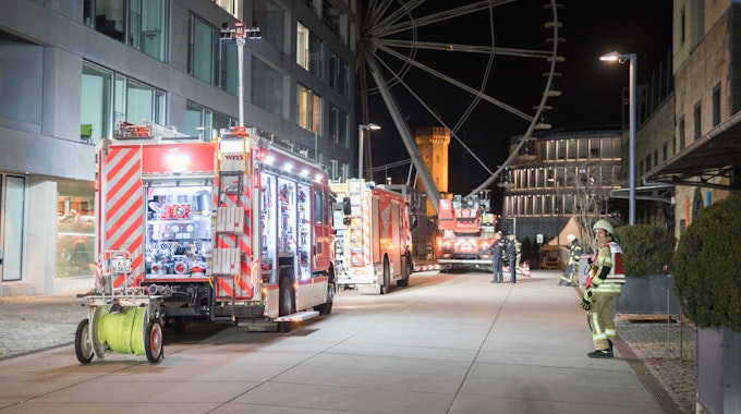 Die Kölner Feuerwehr sichert einen Brand in der Straße "Am Zollhafen" im Kölner Rheinauhafen. Im Hintergrund ist das Riesenrad am Schokoladenmuseum zu sehen.