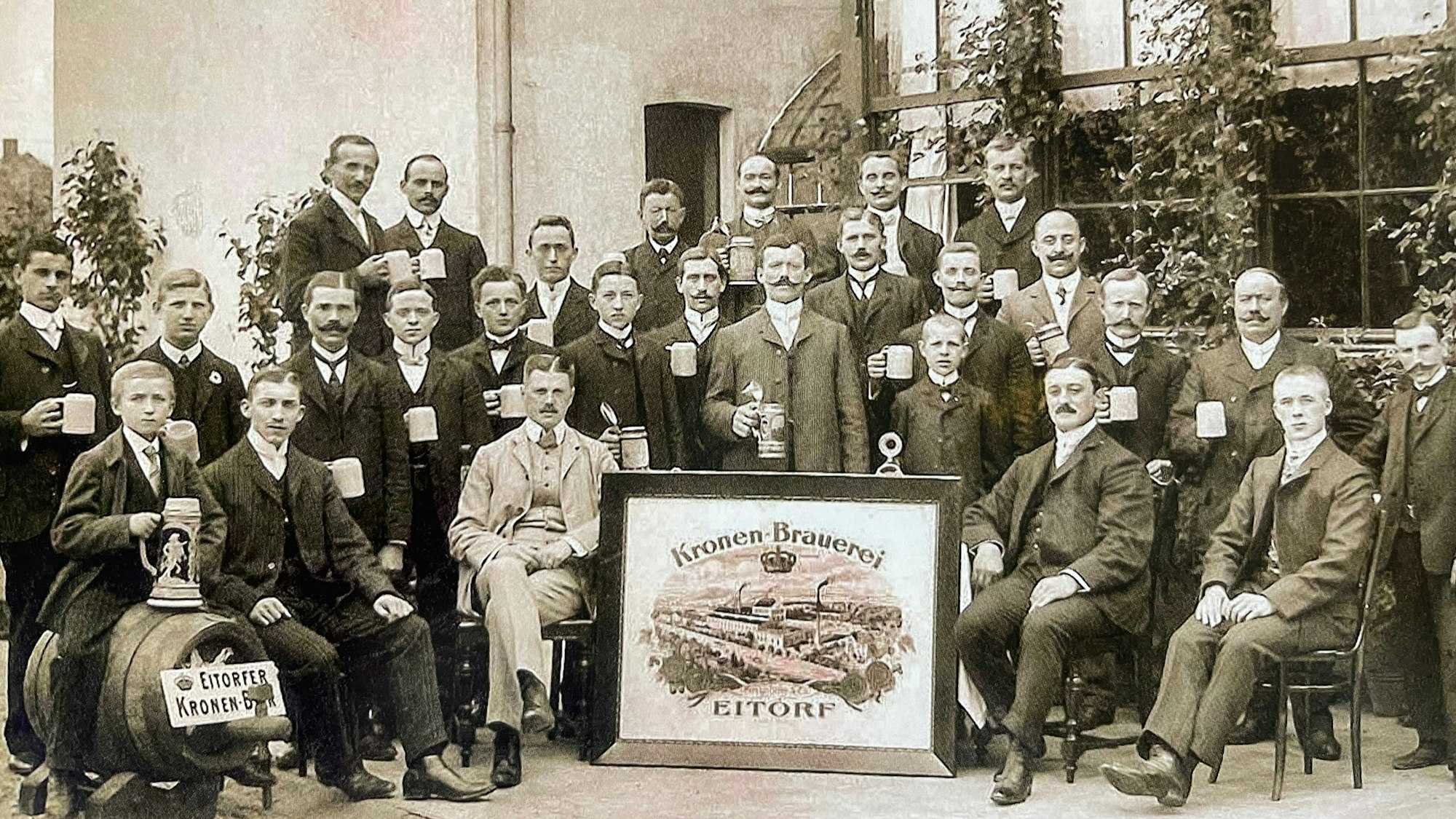 Das Bild zeigt eine Gruppe Männer mit Bierkrügen in der Hand. Sie posieren vor der Brauerei für ein Foto.