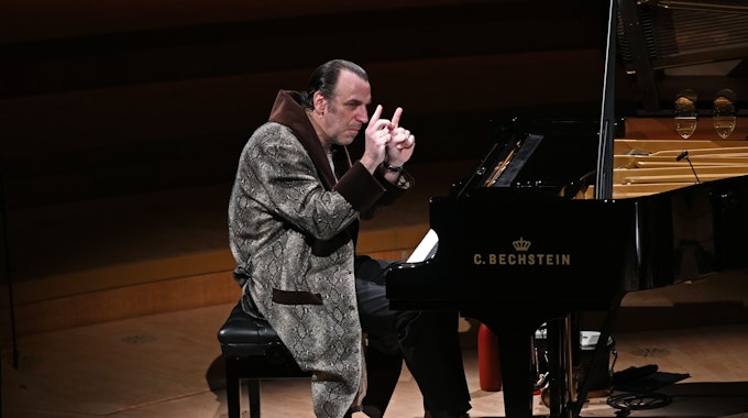 Der kanadische Musiker Chilly Gonzales sitzt am Konzertflügel in der Kölner Philharmonie. Er trägt einen Bademantel und Schlappen.