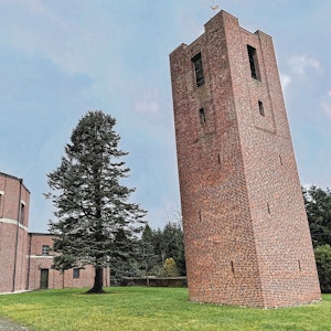 Rechts steht ein hoher, viereckiger Backsteinturm, links ein Rundbau ebenfalls aus Backsteinen. Das Gebäudeensemble liegt in einem kleinen Park, in dem ein hoher Nadelbaum steht.