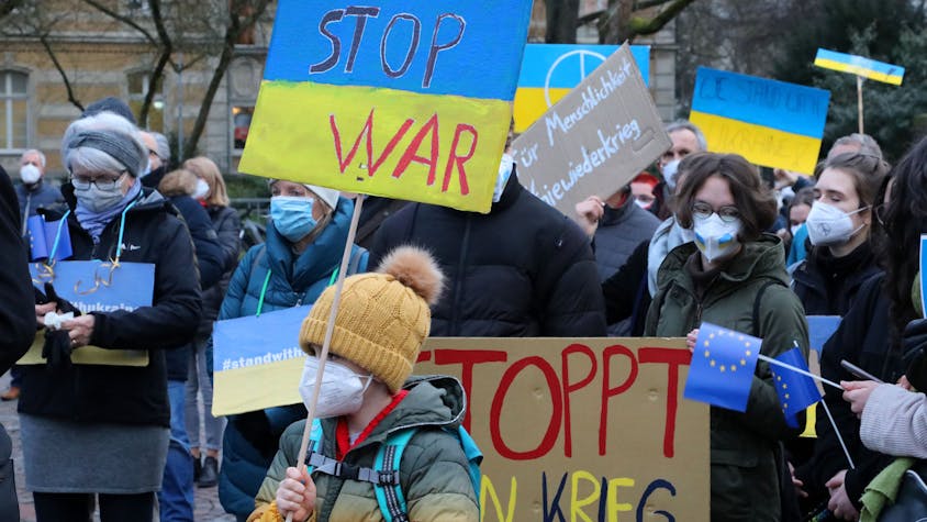 Menschen mit Plakaten auf den "Stop War" und "Stoppt den Krieg" zu lesen ist, stehen bei einer Demonstration gegen den Krieg in der Ukraine auf dem Konrad-Adenauer-Platz in Bergisch Gladbach.