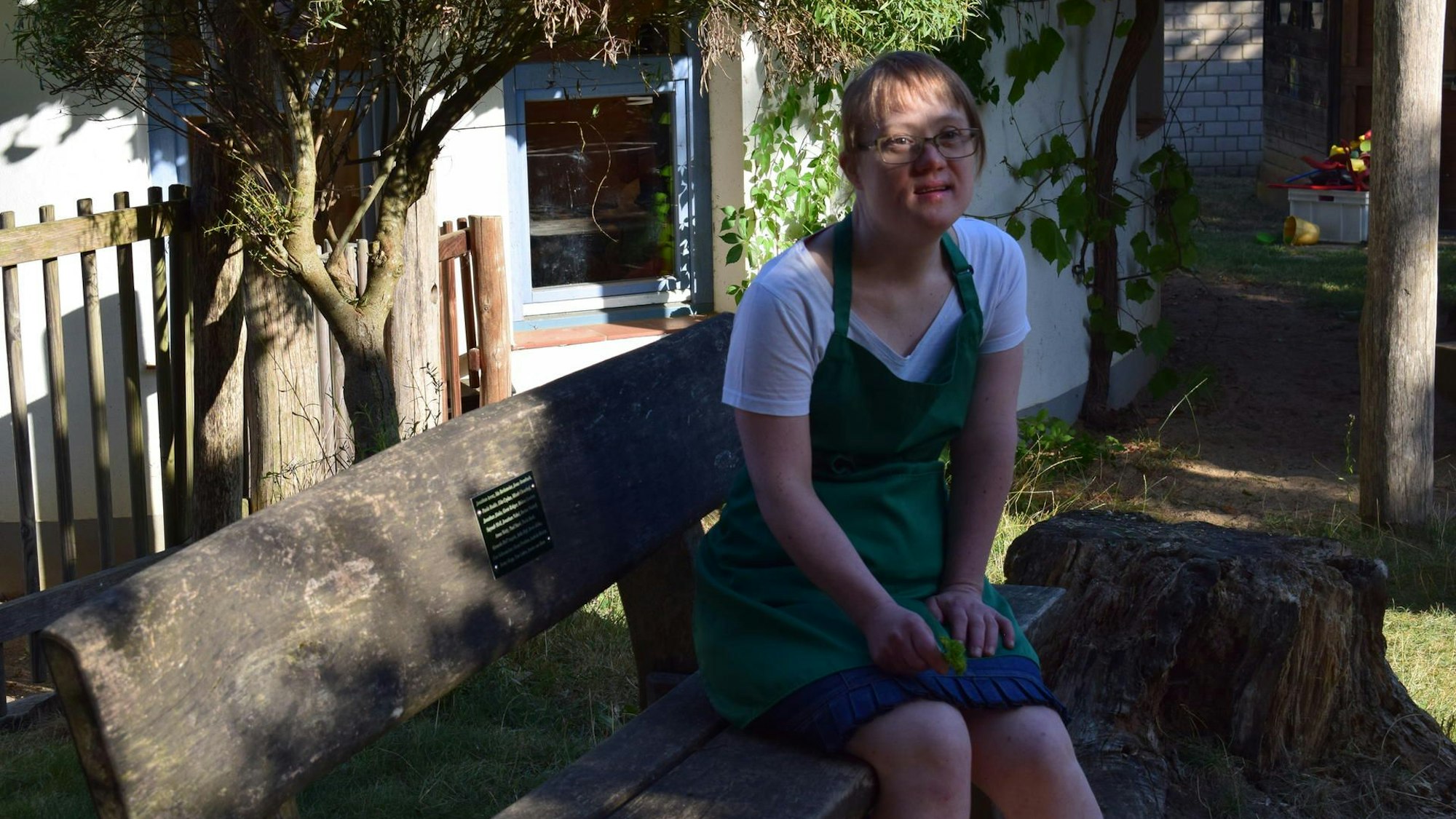 Anna Krechel sitzt auf einer Holzbank, die Hände hat sie in ihren Schoß gelegt.