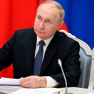 Der russische Präsident Wladimir Putin sitzt auf einem Stuhl. Im Hintergrund ist die russische Flagge zu sehen.