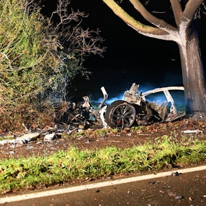 Ein in Teile zerrissenes und ausgebranntes Auto steht an einem Baum.