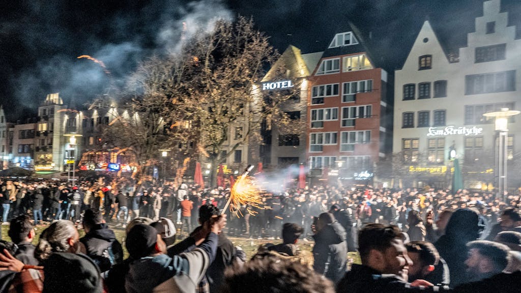 Hunderte Menschen stehen in Köln auf einer großen Platzfläche und zünden Feuerwerk.